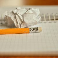 一位在书桌前伏案书写的写作者侧影，桌面散落着练习纸与笔，背景是书架，光线柔和自然
